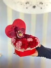 Red heart-shaped Bloom de Fleur box with one deep burgundy orchid atop a bed of red and white-striped carnations.