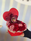 Red heart-shaped Bloom de Fleur box with one deep burgundy orchid atop a bed of red and white-striped carnations.