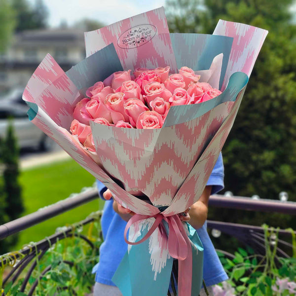 Hand‑tied bouquet of blush pink roses wrapped in pastel teal and pink patterned paper