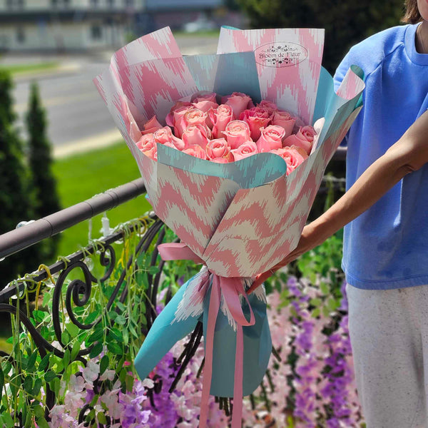 Hand‑tied bouquet of blush pink roses wrapped in pastel teal and pink patterned paper
