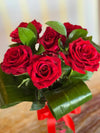 Clear glass vase with red heart pattern and tied red ribbon, holding six deep red roses and folded green leaves.