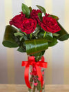 Clear glass vase with red heart pattern and tied red ribbon, holding six deep red roses and folded green leaves.